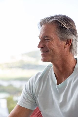 Smiling mature man gazing toward scenic view on terrace, relaxed healthy aging lifestyle