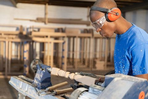 Skilled woodworker shaping decorative spindle on lathe with protective gear in workshop