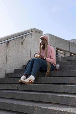 African american woman relaxing on concrete steps eating takeout in urban plaza with iced drink