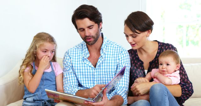 Young family enjoys quality time reading a book together on a couch. Ideal for depicting family bonding, parenting, leisure, home life, and childhood moments. Suitable for family-focused promotions, educational materials, and lifestyle blogs.