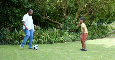 African american father and son practicing soccer drills on backyard lawn, family bonding
