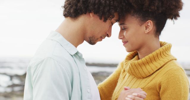 Couple standing close, foreheads touching, sharing tender moment near seashore. Ideal for themes around love, romance, relationships, outdoor settings, emotional connection. Suitable for use in social media posts, greeting cards, relationship advice blogs, wellness articles.