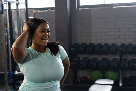 Confident african american woman smiling and posing in gym wearing teal top with wrist tracker