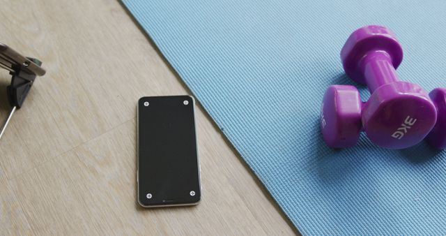 Home exercise setup with a blue yoga mat, purple dumbbells, smartphone, and sunglasses on a wooden floor. Useful for illustrating home fitness routines, relaxation, healthy lifestyle, and personal wellness.