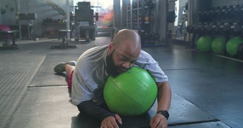 African american man lying on green medicine ball recovering post intensive gym workout