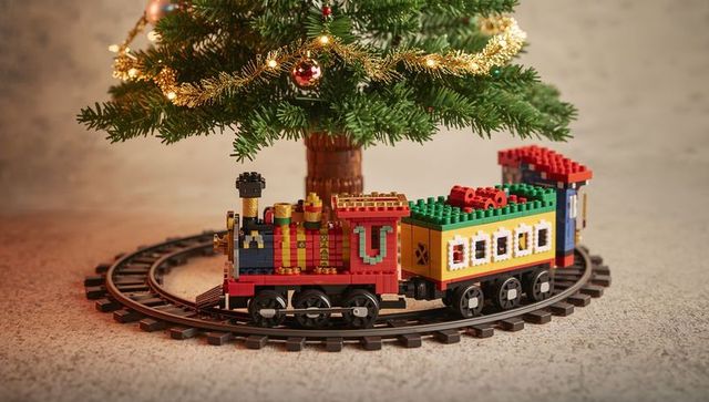 Miniature brick-built toy train circling christmas tree track with warm lights and tinsel