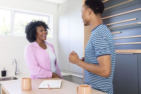 African american couple chatting at modern kitchen island, smiling and holding mugs