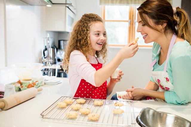 Daughter feeding cookies to her mother in kitchen at home