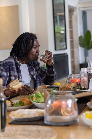 African american friends sharing home dinner around table drinking water enjoying roast chicken