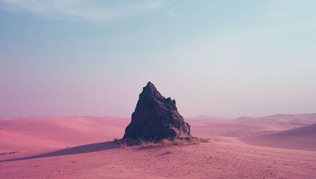 Solitary rock formation in pink desert under clear sky