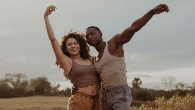 Couple dancing and embracing in meadow at golden hour, raising arms in joyful motion