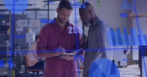 Business colleagues reviewing notebook while analyzing blue data charts in open office
