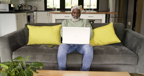 Elderly Man Working from Home Comfortably on Living Room Sofa