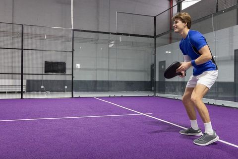 Young man in 20s playing padel on vibrant purple indoor court preparing to strike