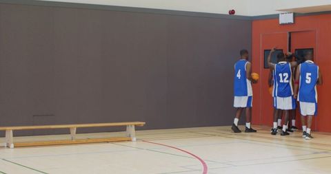 Youth basketball team gathering by gym doors holding basketballs, preparing for practice