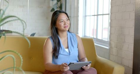 Confident businesswoman reflects while holding tablet in modern office
