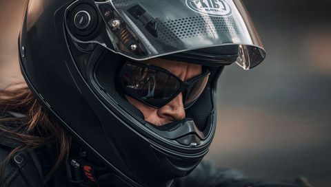 Motorcyclist peering through visor wearing matte black full-face helmet and sunglasses