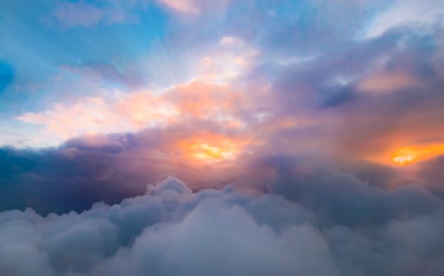 Image shows a breathtaking cloudscape with fluffy clouds bathed in colorful sunlight at sunset. Perfect for use in nature-themed projects, travel promotions, inspirational quotes, weather forecasts, or background elements for presentations and websites.
