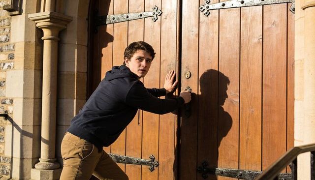 Young man turning heavy wooden door handle at historic stone archway