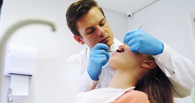 A Caucasian male dentist is examining the teeth of a young Caucasian female patient in a dental clinic, with copy space. His focused attention and her relaxed demeanor suggest a professional and comfortable healthcare environment.