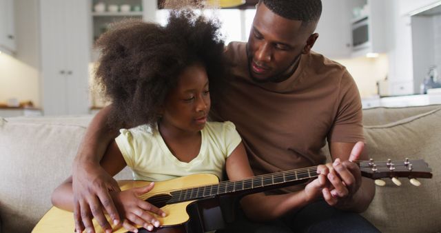 Father showing his daughter how to play the acoustic guitar in their living room, ideal for content related to parenting, family bonding, learning music, and father-daughter relationships.