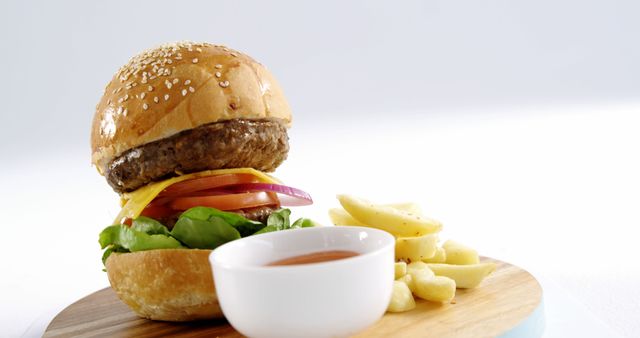 A juicy cheeseburger with lettuce, tomato, and onions is paired with a side of fries and a dipping sauce, presented on a wooden board with copy space. Perfect for highlighting a classic American meal or promoting a casual dining experience.