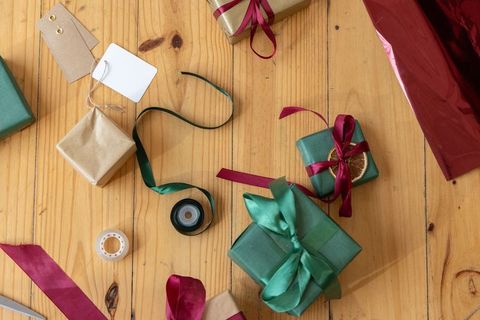 Green gift wrapping flatlay with satin ribbons, kraft tags and tape on wooden table