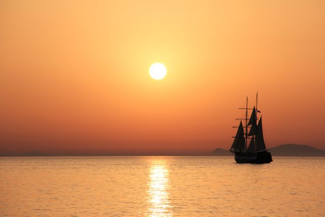 Sailboat silhouetted against an orange sunset on a calm ocean, perfect for travel blogs, adventure articles, and campaign posters promoting peace and relaxation.