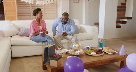 African American couple celebrating in cozy living room with purple balloons and cupcakes
