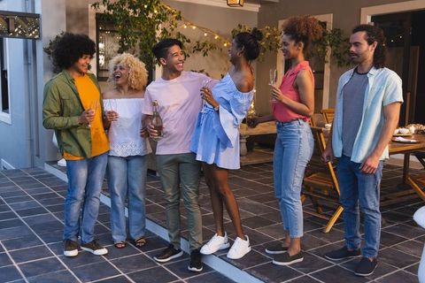 Group celebrating on terrace pouring champagne and toasting at evening outdoor party