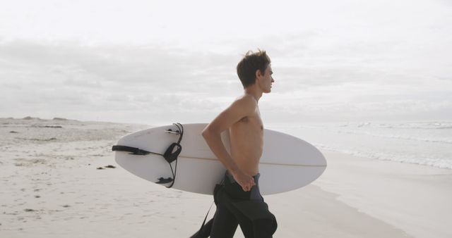 Young man carrying surfboard on sandy beach at dawn - Download Free Stock Images Pikwizard.com