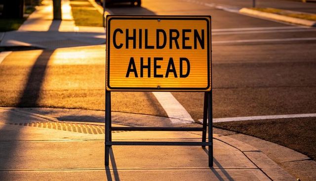 Children ahead warning sign on sidewalk at sunset casting long shadows, school zone safety