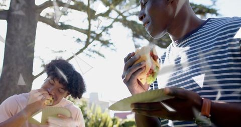 Young Friends Eating Burgers in Sunlit Park Picnic Casual Outdoor Summer Lunch