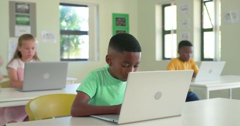 Elementary students using laptops in bright classroom focused on digital learning engagement