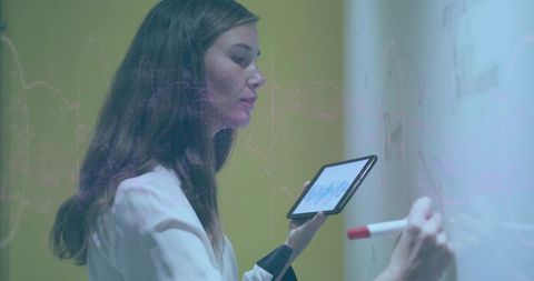 Businesswoman writing on whiteboard holding tablet for digital presentation and planning