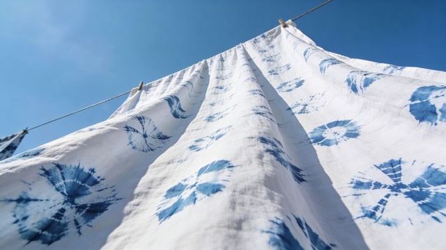 Sunlit tie-dye linen billowing on rooftop clothesline with indigo shibori circles