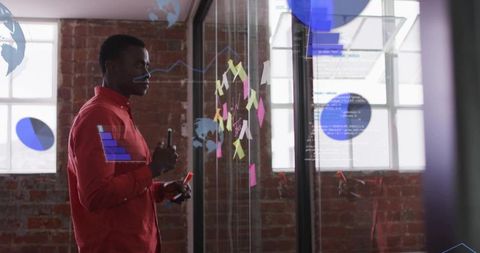 Strategist brainstorming on glass wall with post-it notes and digital data overlays