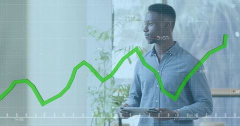 African American businessman standing in modern office holding tablet with digital display overlay of financial graphs in foreground, symbolizing data analysis and strategic planning. Useful for illustrating business and financial reporting, tech solutions, economic trends, or innovation in the workplace themes.