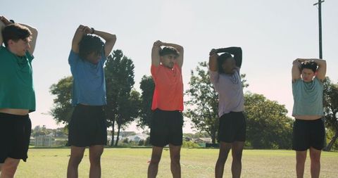 Diverse male teammates warming up outdoors stretching triceps and preparing for training