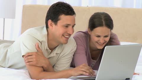 Joyful Couple Relaxing on Bed Using Laptop at Home