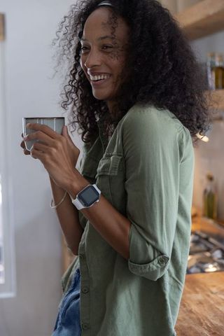 Smiling african american woman holding mug checking smartwatch in cozy morning kitchen