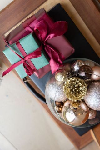 Stacked teal burgundy gift boxes with gold baubles and pinecone bowl holiday flatlay