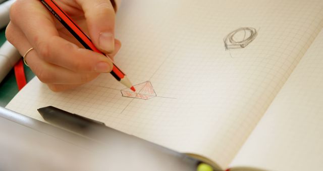 A person is sketching geometric shapes on graph paper, with copy space. Their focus on drawing suggests a task involving precision, related to education or design work.