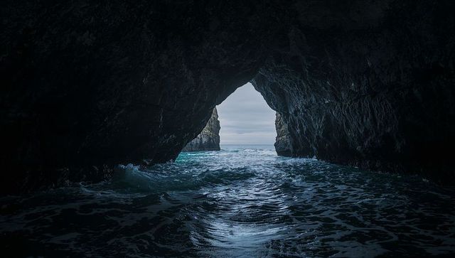 Triangular sea cave framing moody blue ocean with churning water and rugged rock walls