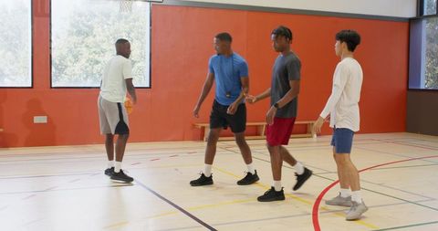 Male players practicing basketball drills on indoor hardwood court during training session
