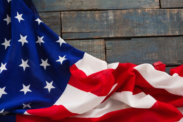 This image captures a close-up view of the American flag draped over a rustic wooden table. Ideal for use in patriotic themes, national holidays like Independence Day and Memorial Day, or any content celebrating American culture and pride. The wooden background adds a vintage and rustic feel, making it suitable for historical or traditional contexts.