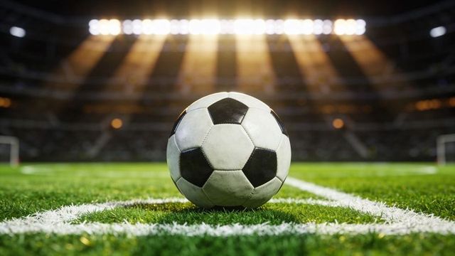 Classic black and white soccer ball resting on goal line under glowing stadium floodlights