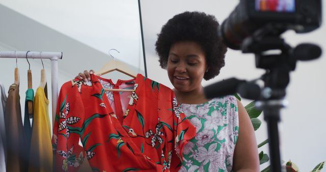 Young African American female fashion influencer recording a video review of a brightly patterned red dress. Perfect for use in content marketing, digital content creation tutorials, fashion blog articles, influencer strategy visuals, and online retail promotions.
