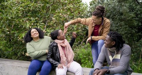Friends laughing and playfully interacting on bench in leafy city park
