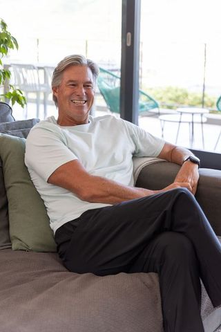 Senior man relaxing and smiling on modern sofa by sliding glass door
